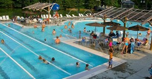 Una piscina con varias pistas, tumbonas y sombrillas.