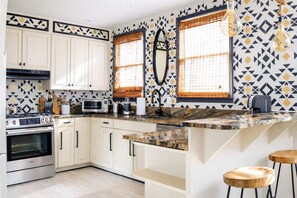 Una cocina moderna con armarios blancos, encimera de granito, horno empotrado, microondas y cafetera.