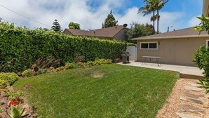 A residential backyard with a well-maintained lawn, a patio area, and a variety of plants and shrubs. - Perfect Location | Fantastic Home | Near Beach! (Oceanside)