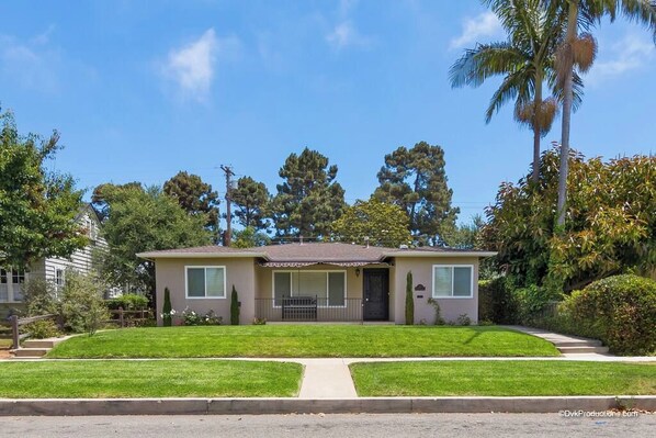 A single-story house with a front porch, a small front yard, and a palm tree to the right.