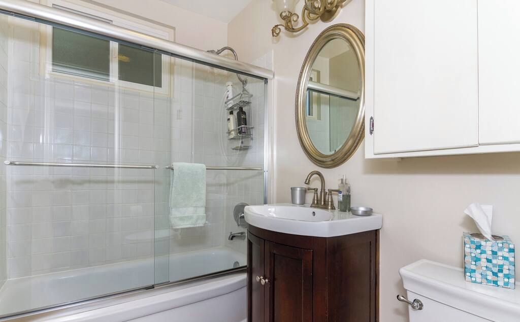 A bathroom with a glass-enclosed shower, a white sink, a wooden vanity, and a toilet.