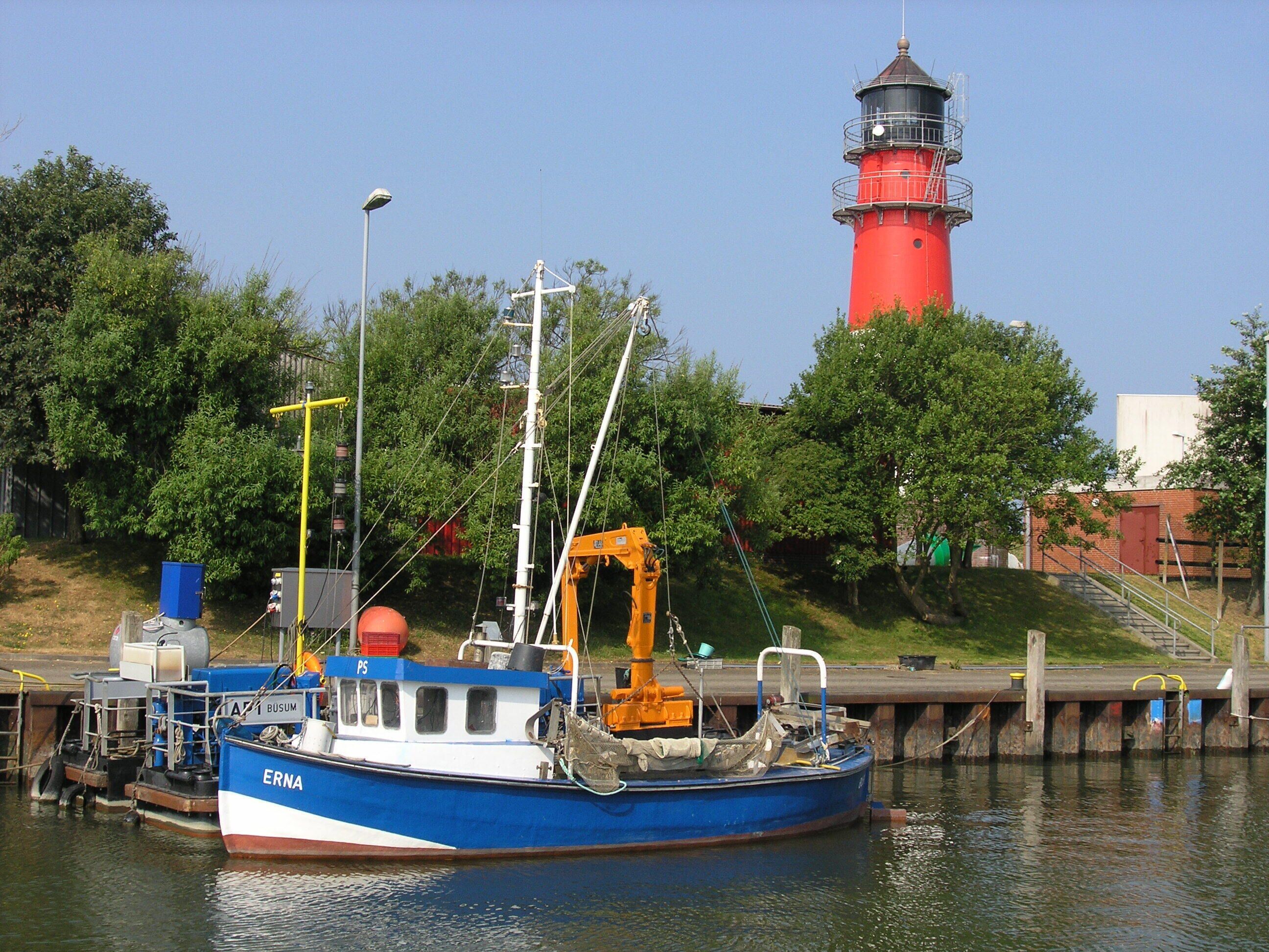 A blue boat docked at a pier with a red lighthouse in the background.