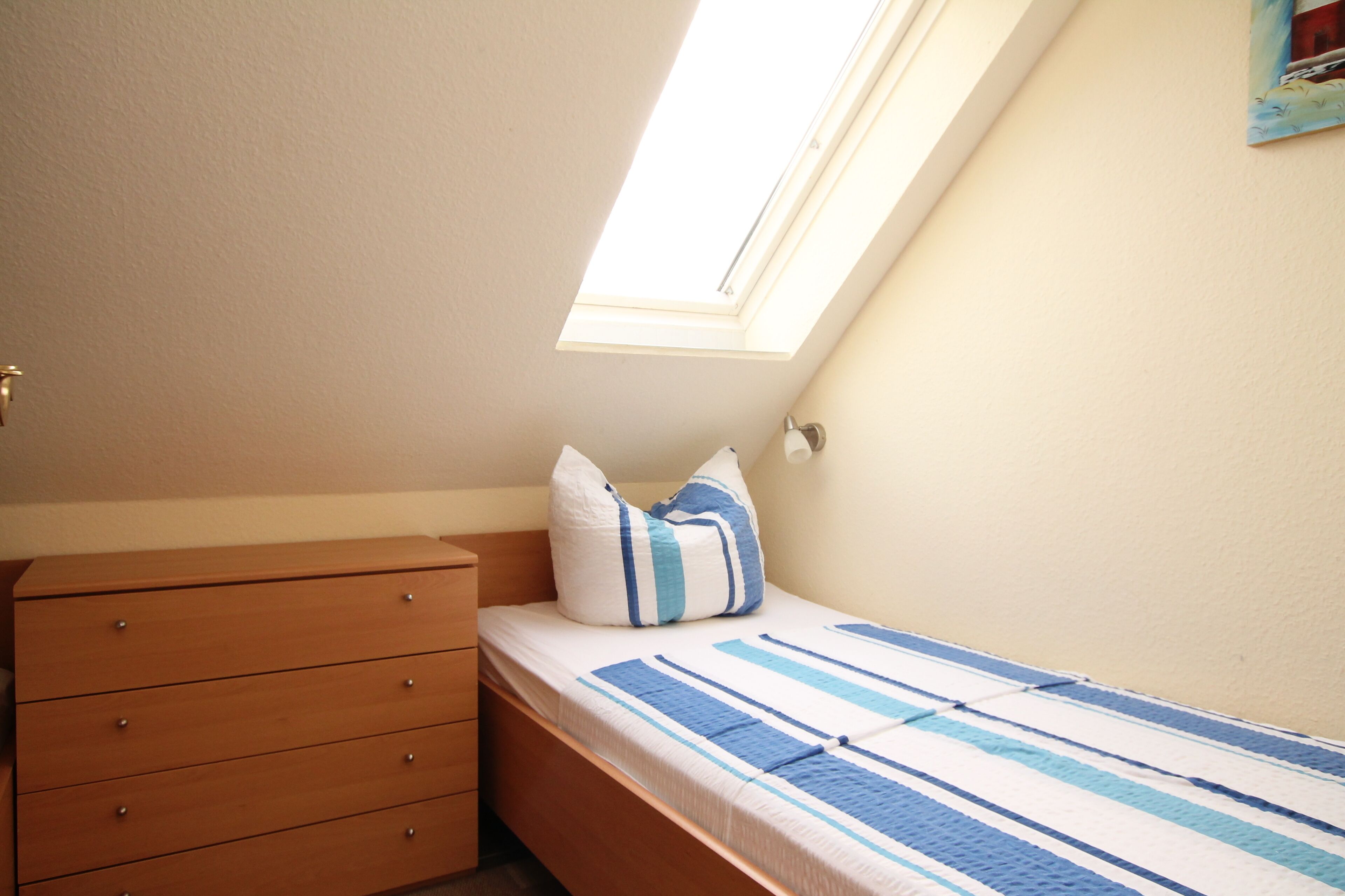 A bedroom with a skylight, a wooden dresser, and a bed with striped bedding.