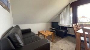 Una sala de estar con un sofá de cuero negro, una mesa de centro de madera, un televisor y un comedor con una mesa y sillas.