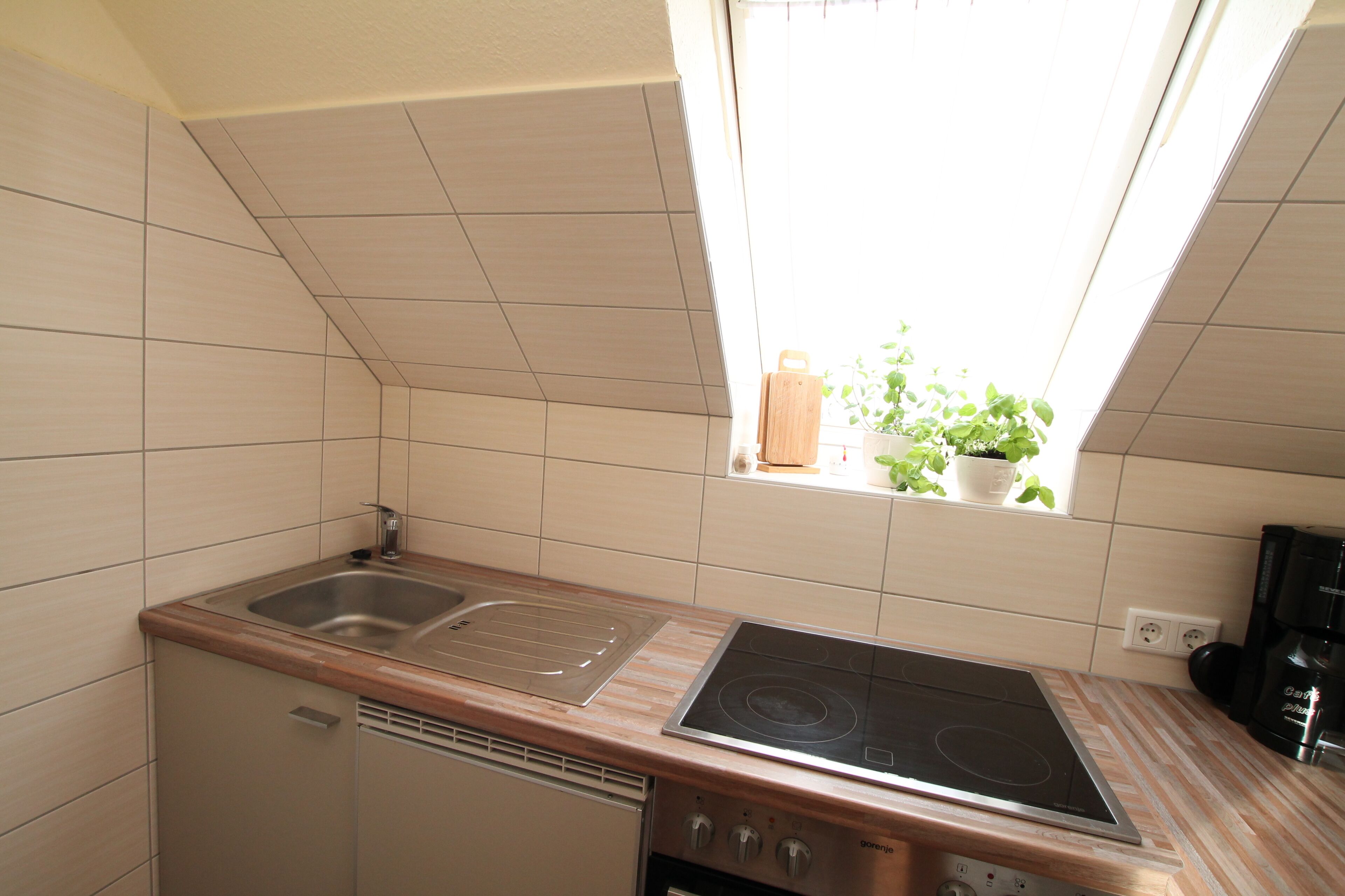 Une cuisine compacte équipée d’un évier, d’une cuisinière et d’une fenêtre donnant sur un espace verdoyant.
