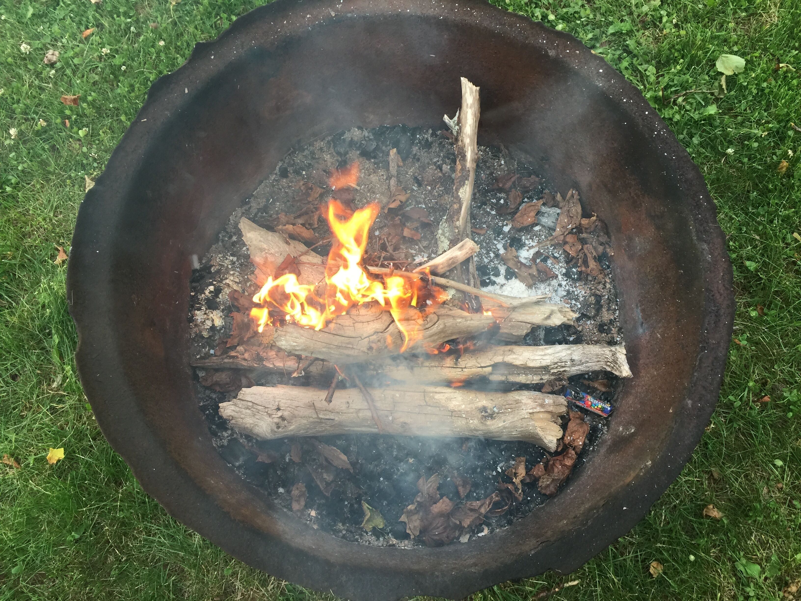 Ein Lagerfeuer mit brennenden Holzscheiten und Glut auf einer Rasenfläche.