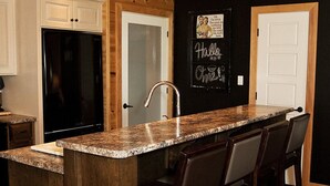 A kitchen with a central island, bar stools, wooden cabinets, a black refrigerator, and a chalkboard with a message. - Relax, Connect & Enjoy with AC at private Oasis. (Long Creek)