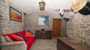 A rustic room with stone walls, a wooden door, a red sofa, a wooden chest, and a hanging lantern. - Celler Colltor (Santa Maria d'Oló)