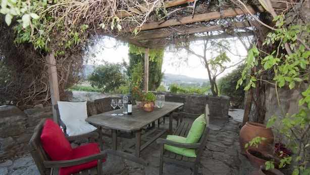 An outdoor patio with a wooden table and chairs, surrounded by stone walls and greenery. - Celler Colltor (Santa Maria d'Oló)