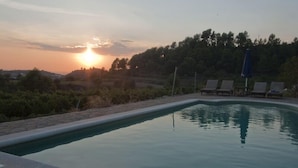A swimming pool with lounge chairs and an umbrella, surrounded by trees and hills during sunset. - Celler Colltor (Santa Maria d'Oló)