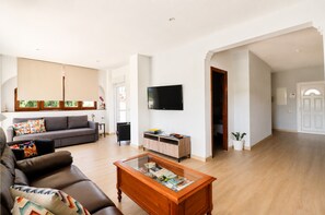 Un salon spacieux comprenant un canapé, une table basse, un téléviseur et une porte donnant sur une autre pièce.