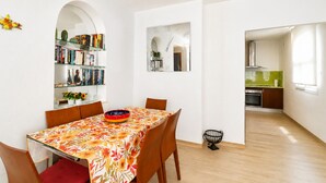Zona pranzo con tavolo, sedie, una libreria e una cucina sullo sfondo.