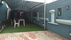 A covered patio area with artificial grass, a table and chairs, and a brick pathway. - D'Luxx Villa & Suites (Lagos)