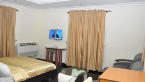 A hotel room with a bed, a desk, a chair, a television, and curtains. - D'Luxx Villa & Suites (Lagos)