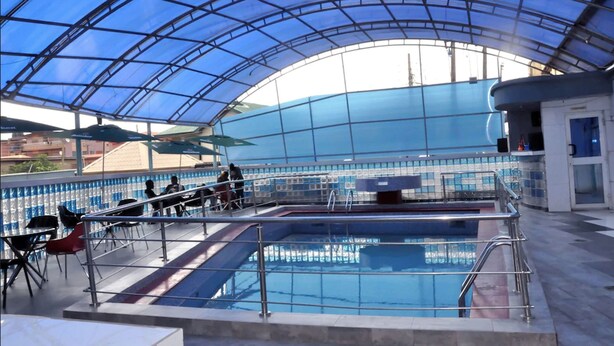 An indoor swimming pool with a glass ceiling, surrounded by chairs and a poolside area. - D'Luxx Villa & Suites (Lagos)
