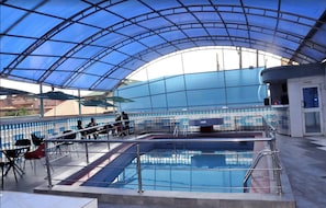 An indoor swimming pool with a glass ceiling, surrounded by chairs and a poolside area. - D'Luxx Villa & Suites (Lagos)
