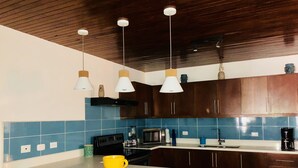 Uma cozinha com armários de madeira escura, azulejos azuis, bancada branca e três banquetas azuis.