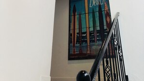 Uma escadaria com corrimão preto, teto de madeira e luminária fixada na parede.