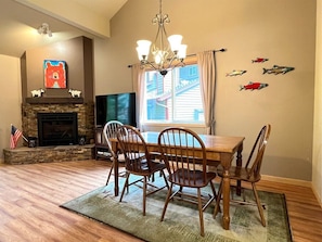 A dining area with a wooden table and chairs, a fireplace, a television, and decorative fish on the wall.