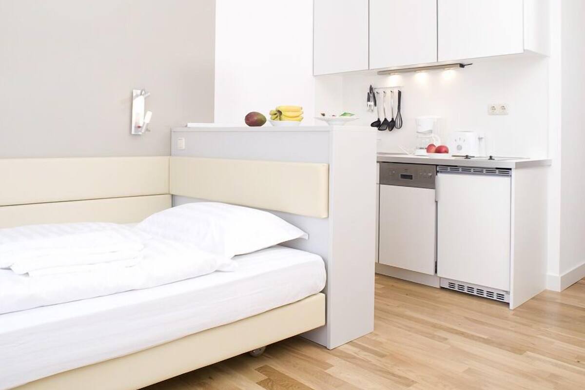 A modern bedroom with a bed, a small kitchenette with a coffee maker, and a white wardrobe.