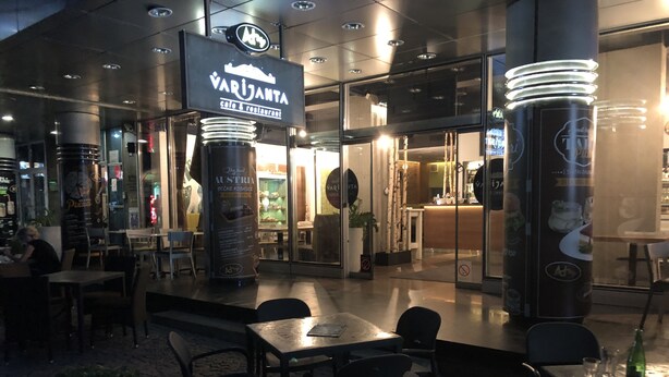An outdoor dining area with tables and chairs, a sign for 'VARJANTA cafe & restaurant', and a glass wall separating the dining area from the interior. - Apartment Markovic (Belgrade)