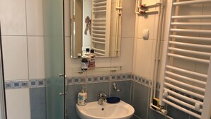 A bathroom with a glass shower enclosure, a white sink, a mirror, and a towel rack. - Apartment Markovic (Belgrade)