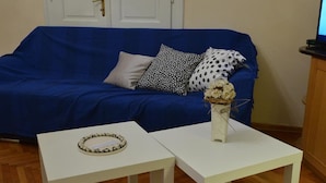 A room with a blue sofa, two white tables, and a vase with flowers. - Apartment Markovic (Belgrade)