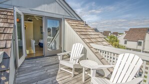 Ett trädäck med två vita Adirondack-stolar och en glasdörr som leder in till ett rum.