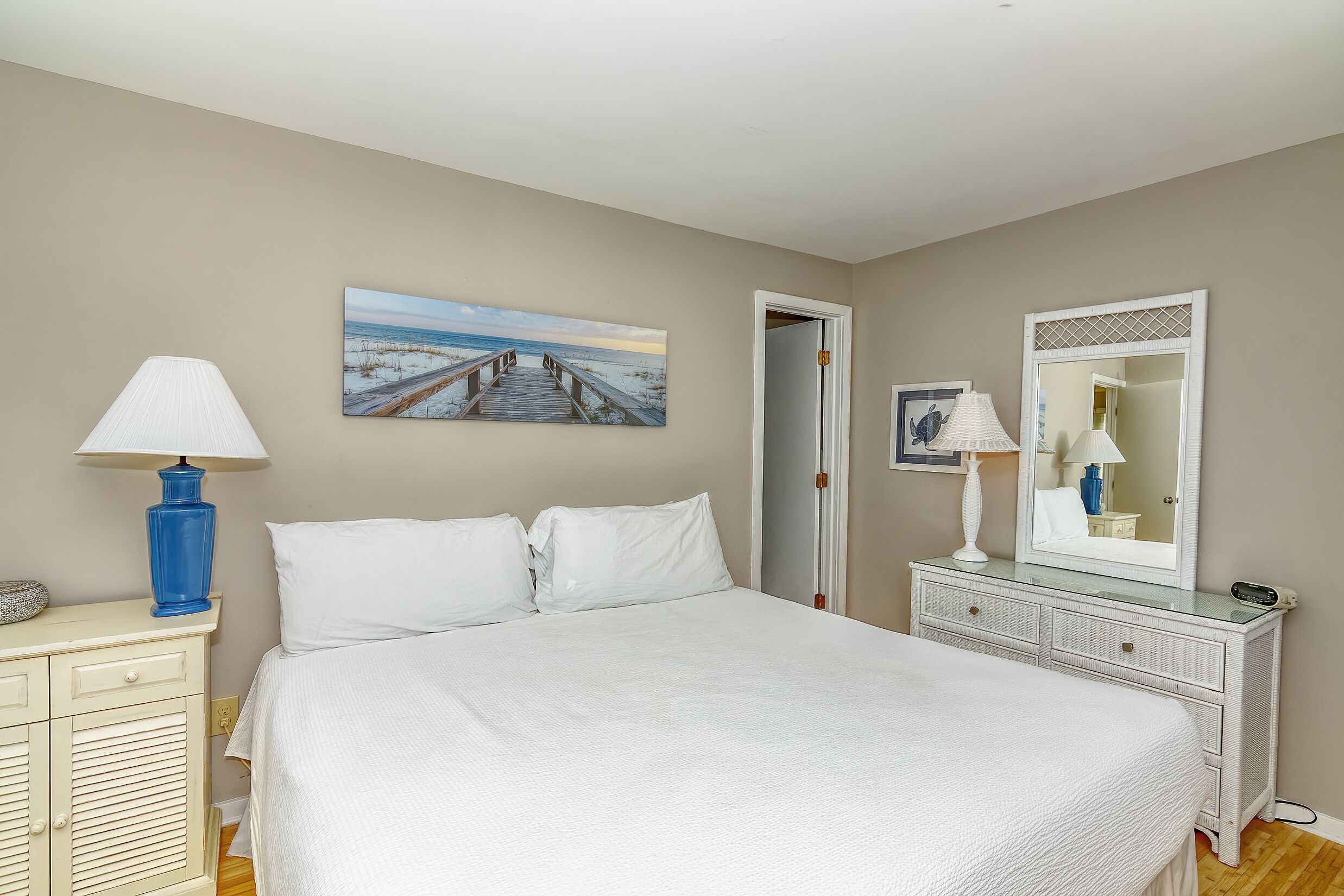 A bedroom with a bed, a dresser, a lamp, a painting, and a mirror.