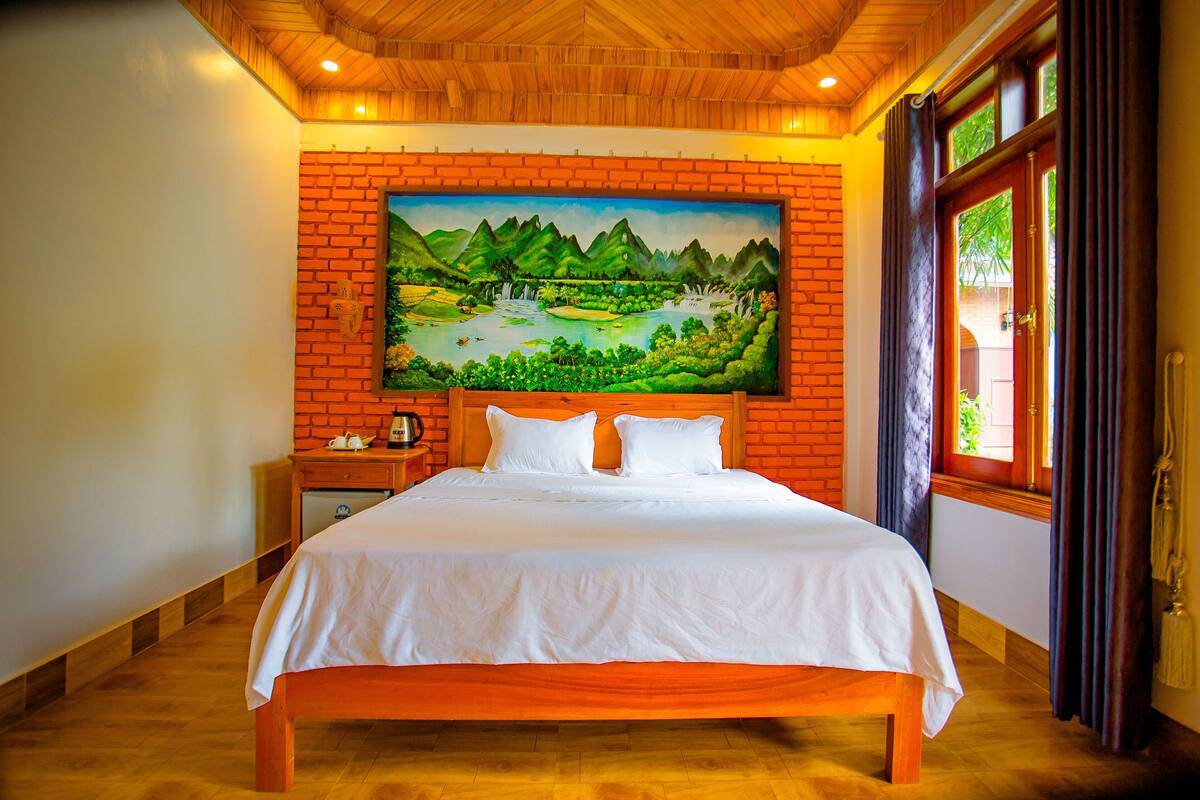 A room with a large bed, a brick wall, and a painting of a landscape.