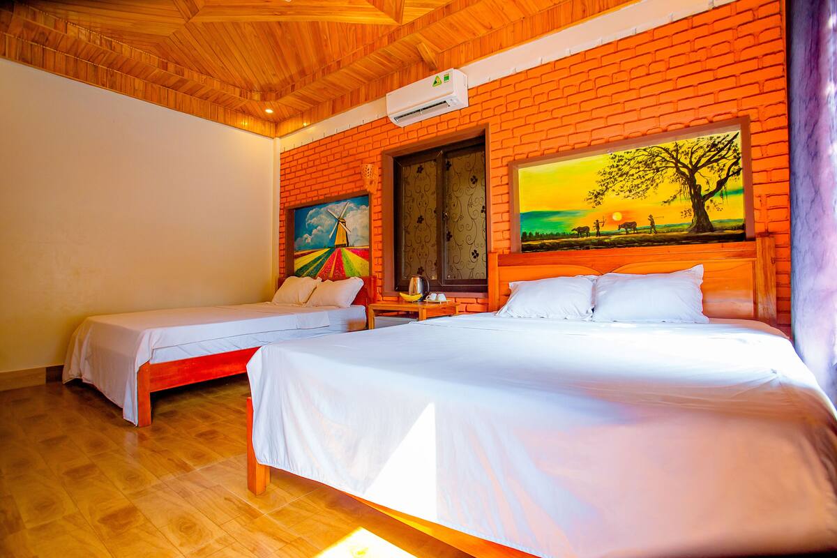 A room with two beds, a brick wall, and a painting of a sunset.