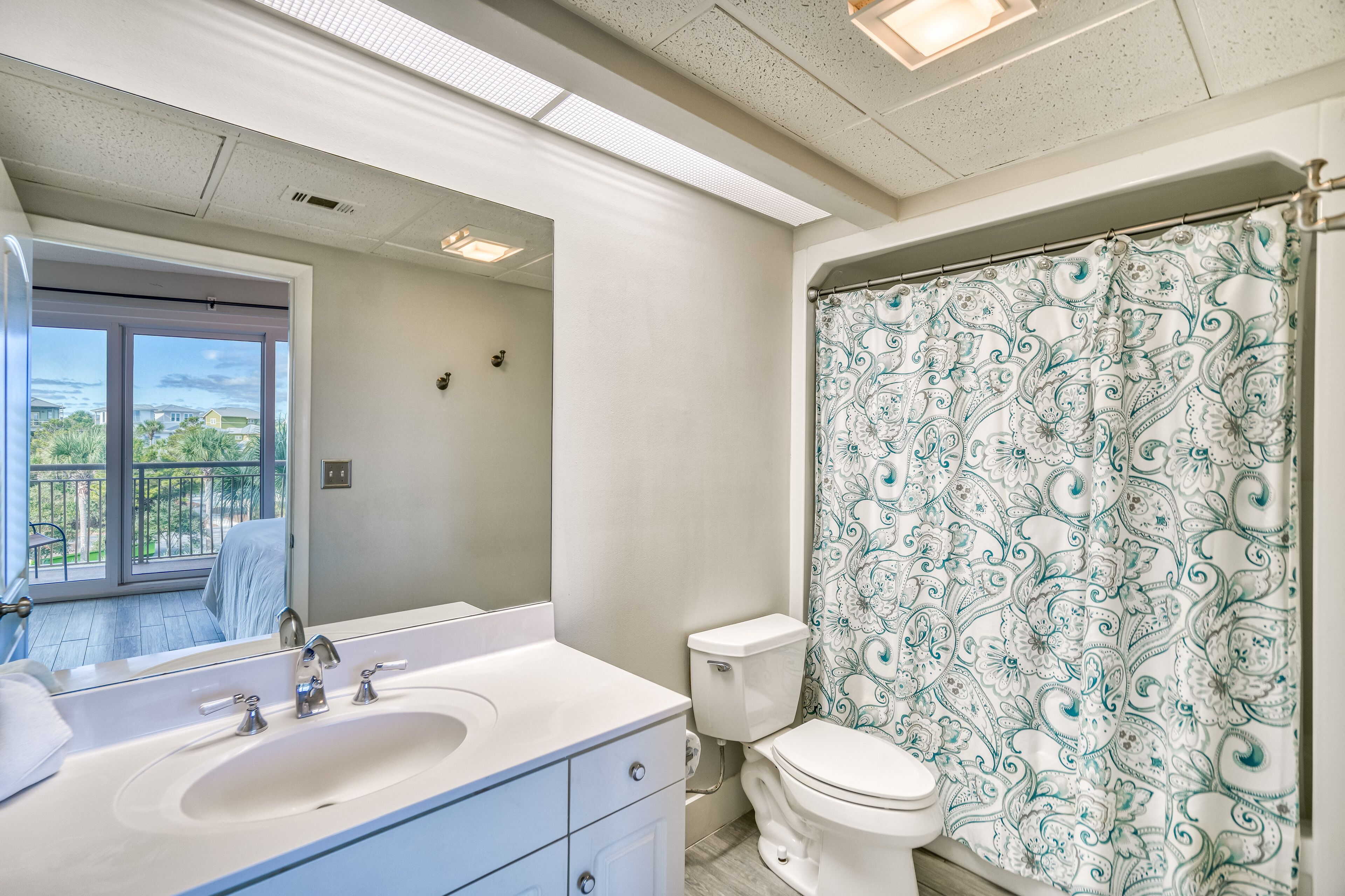 A bathroom with a large mirror, a sink, a toilet, and a shower curtain with a paisley pattern.