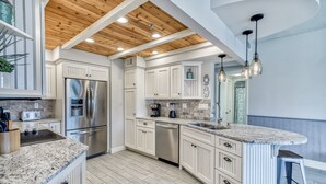 Una cocina moderna con armarios blancos, electrodomésticos de acero inoxidable, encimera de granito y techo de madera.