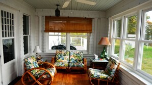 A sunroom with wooden flooring, wicker furniture, and large windows. - Classic and Spacious Maine Waterfront Retreat (Sullivan)