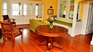 A dining area with a wooden table and chairs, a green sofa, and a window seat with a view. - Classic and Spacious Maine Waterfront Retreat (Sullivan)