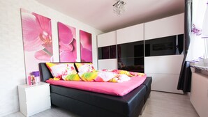 Une chambre moderne avec un lit noir, une literie aux couleurs vives et une grande œuvre d’art florale accrochée au mur.