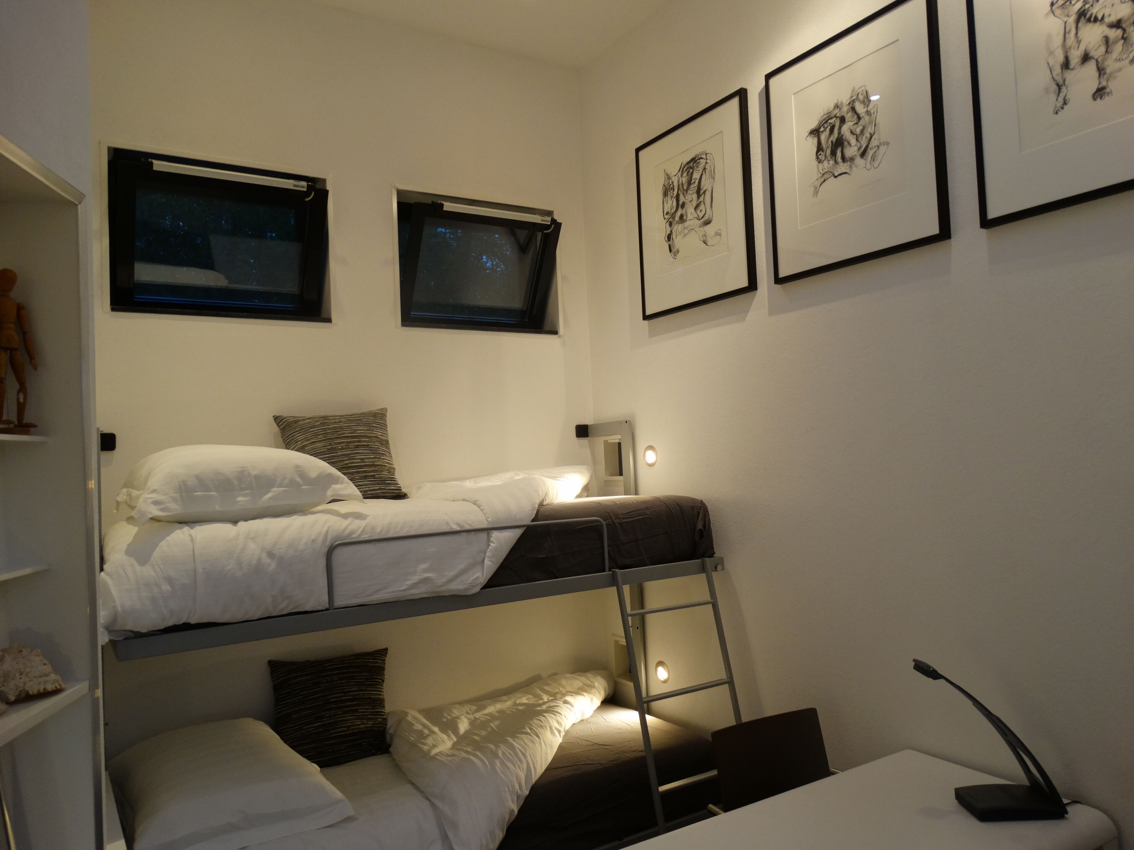 Ein Schlafsaalzimmer mit Etagenbetten, einem Schreibtisch, einem Stuhl und gerahmten Bildern an den Wänden.