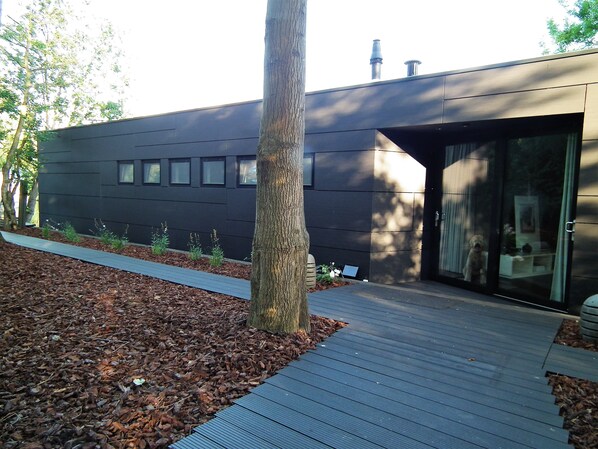 A modern building with a dark facade, a wooden deck, and a tree in the foreground. - A Stunning Contemporary Designed Houseboat. (Giethoorn)
