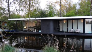 A modern house with a flat roof, large windows, and a balcony overlooking a body of water.