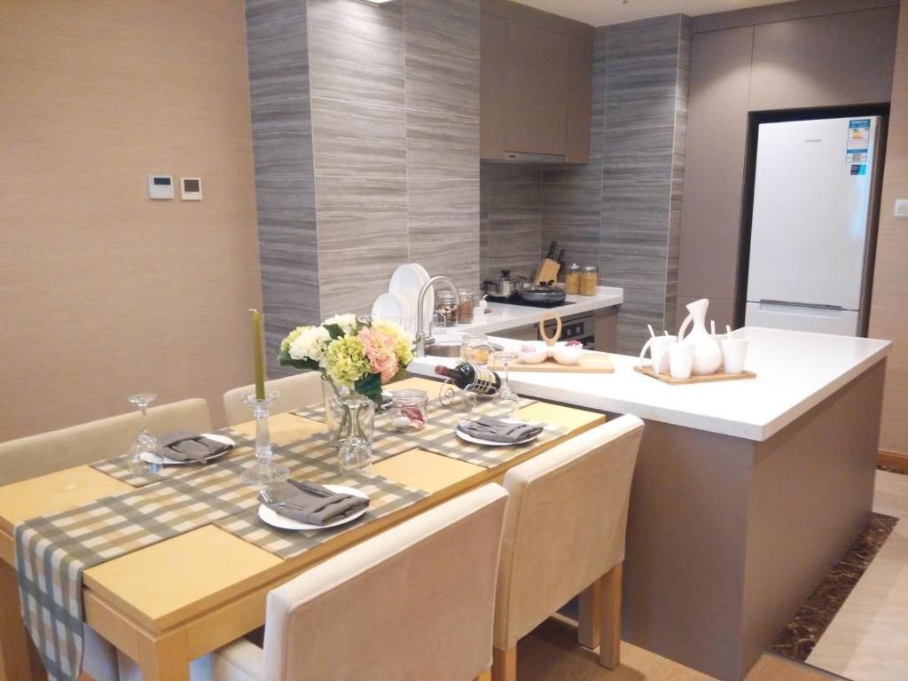 A modern kitchen with a central island, a dining area with a table set for two, and a refrigerator in the background.