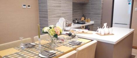 A modern kitchen with a central island, a dining area with a table set for two, and a refrigerator in the background.