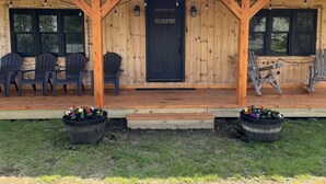 A wooden porch with black Adirondack chairs, a black door, and two potted plants. - Cozy Cabin in Pittsburg NH  - DIRECT SNOWMOBILE & ATV TRAIL ACCESS (Pittsburg)