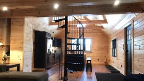 A cozy cabin interior with a wooden interior, a spiral staircase, a kitchen area, and a seating area with a sofa and a table. - Cozy Cabin in Pittsburg NH  - DIRECT SNOWMOBILE & ATV TRAIL ACCESS (Pittsburg)