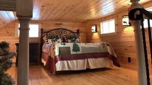 A cozy cabin bedroom with a wooden ceiling, a bed with a forest-themed bedspread, and two wall-mounted windows with decorative lights. - Cozy Cabin in Pittsburg NH  - DIRECT SNOWMOBILE & ATV TRAIL ACCESS (Pittsburg)