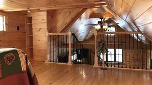 A wooden interior with a sloped ceiling, a staircase, and a bed with a green and red blanket. - Cozy Cabin in Pittsburg NH  - DIRECT SNOWMOBILE & ATV TRAIL ACCESS (Pittsburg)