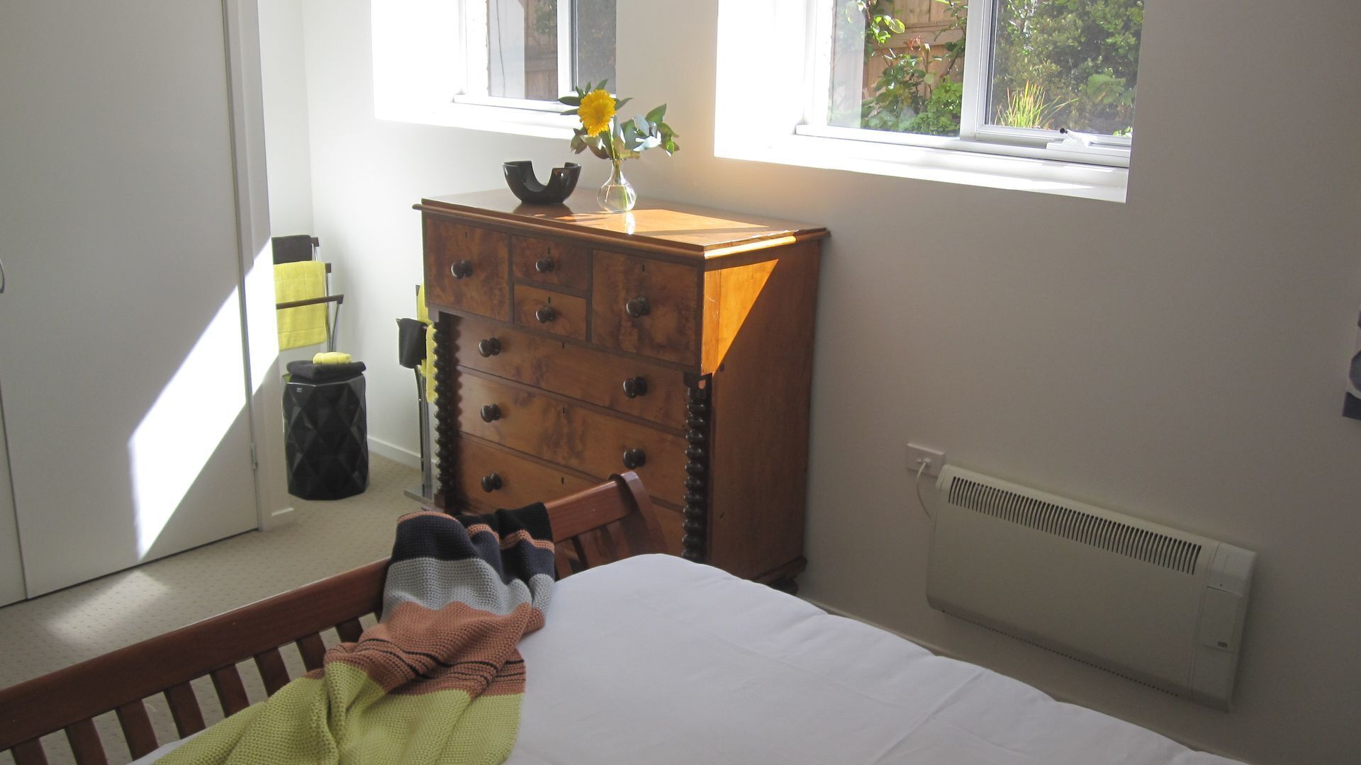 Un dormitorio con cama, cómoda de madera, radiador y ventana con vistas a vegetación.