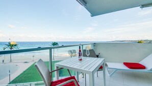 A balcony with a white table and red cushioned chairs, overlooking a beach and ocean. - Sa Maniga - sunny modern apartment, 3floors, on the beach up to 3per. WLAN incl. (Cala Millor)