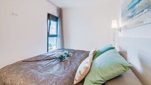 A bedroom with a bed, a window, a painting, and a wall-mounted lamp. - Sa Maniga - sunny modern apartment, 3floors, on the beach up to 3per. WLAN incl. (Cala Millor)