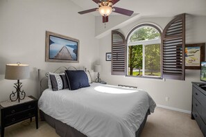 Quarto com uma cama, janela com persianas, ventilador de teto e mesa de cabeceira com abajur.