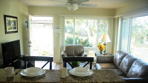 A living room with a television, a dining area with a table set for two, and a large window with a view of the outdoors.